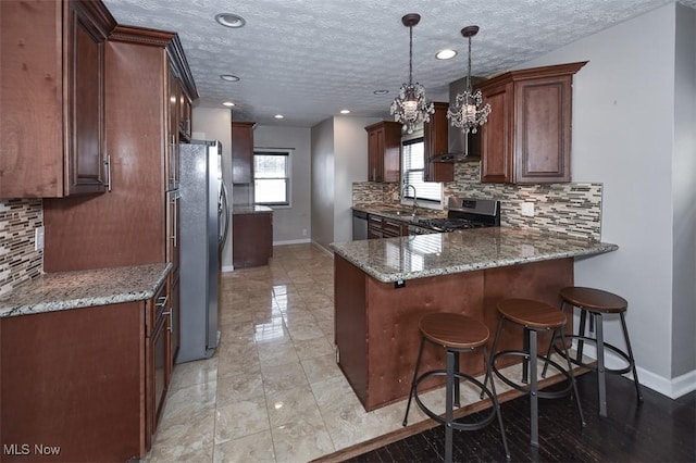 kitchen featuring decorative light fixtures, appliances with stainless steel finishes, stone countertops, and kitchen peninsula