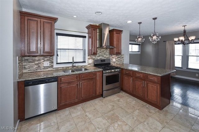 kitchen with wall chimney exhaust hood, stainless steel appliances, pendant lighting, sink, and kitchen peninsula