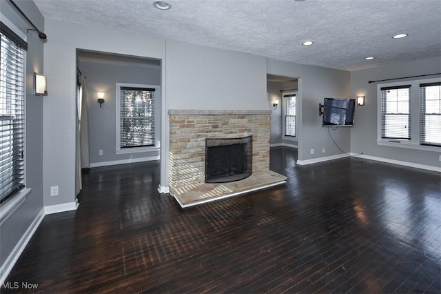 unfurnished living room featuring dark wood-type flooring, a stone fireplace, and a textured ceiling