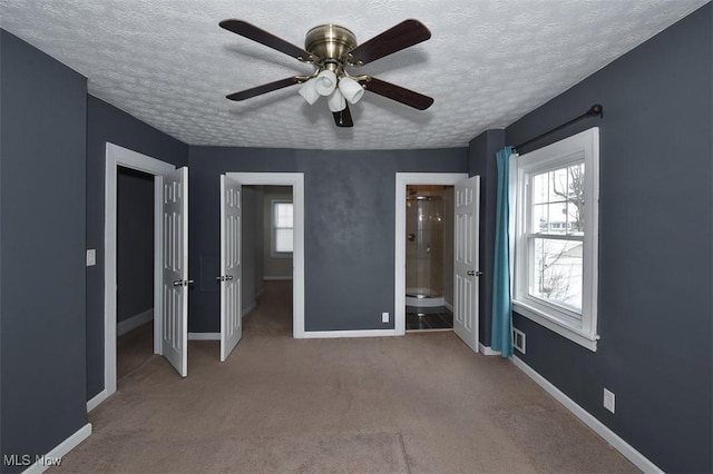 unfurnished bedroom featuring multiple windows, a textured ceiling, connected bathroom, and light colored carpet