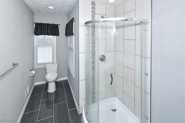 bathroom featuring a shower with door, toilet, and a textured ceiling