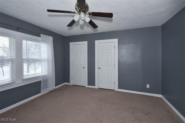 unfurnished bedroom featuring ceiling fan, carpet floors, a textured ceiling, and two closets