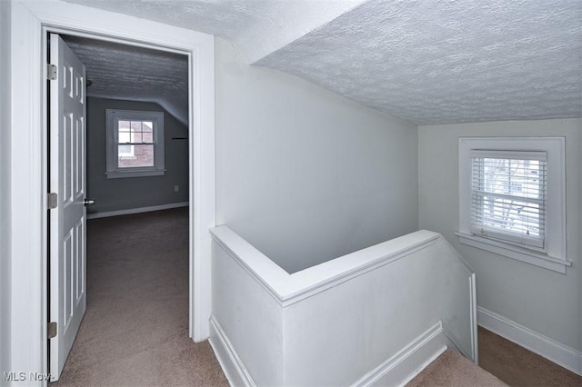 hall featuring carpet floors, vaulted ceiling, and a textured ceiling