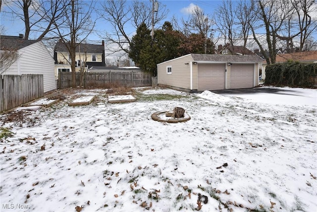 yard covered in snow featuring a garage, a fire pit, and an outbuilding