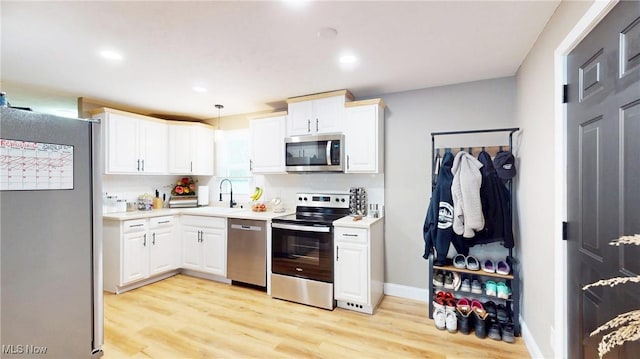 kitchen featuring appliances with stainless steel finishes, decorative light fixtures, light hardwood / wood-style floors, sink, and white cabinetry