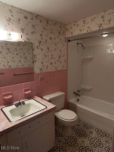 full bathroom featuring washtub / shower combination, tile patterned flooring, toilet, tile walls, and vanity