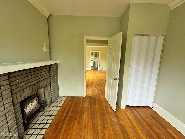 unfurnished living room featuring hardwood / wood-style flooring, crown molding, and a brick fireplace