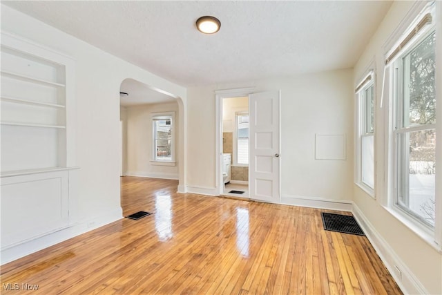 unfurnished room with light hardwood / wood-style flooring, built in shelves, and a textured ceiling