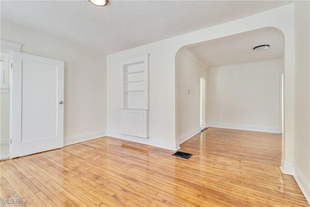 spare room with light wood-type flooring, a textured ceiling, and built in features