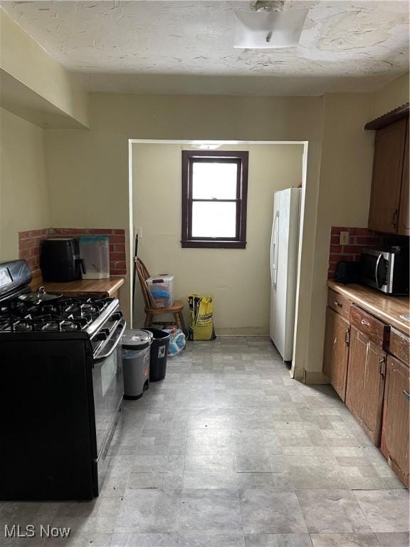 kitchen featuring a textured ceiling, white fridge, and black range with gas cooktop