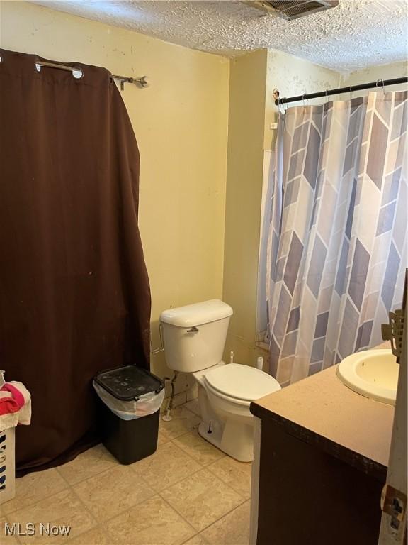 bathroom with toilet, tile patterned floors, vanity, and a textured ceiling