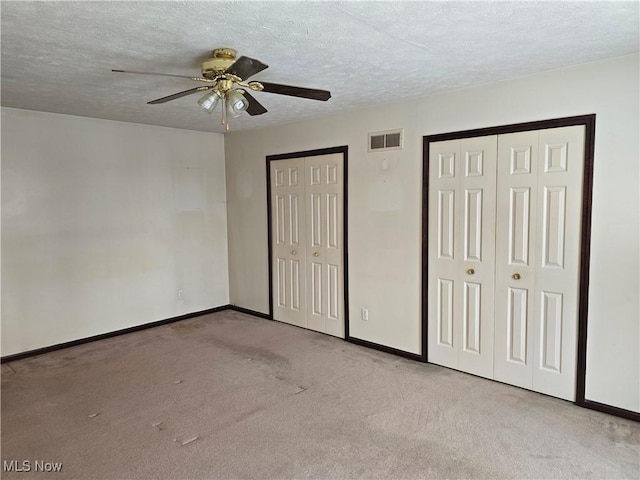 unfurnished bedroom featuring light carpet, a textured ceiling, visible vents, and multiple closets