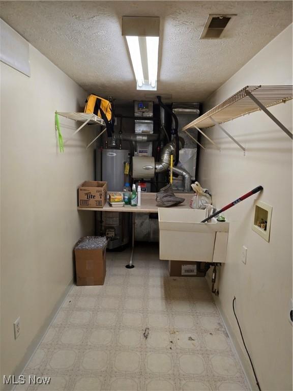 interior space featuring gas water heater, a sink, a textured ceiling, and light floors