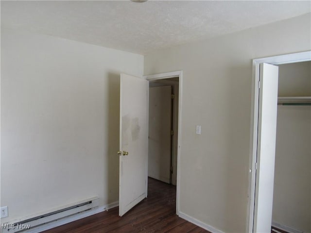 unfurnished bedroom with baseboard heating, dark wood-type flooring, a closet, and a textured ceiling