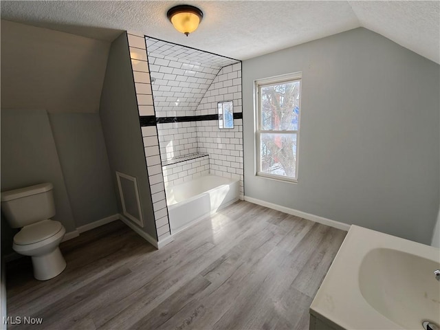 bathroom with a washtub, hardwood / wood-style flooring, a textured ceiling, and lofted ceiling