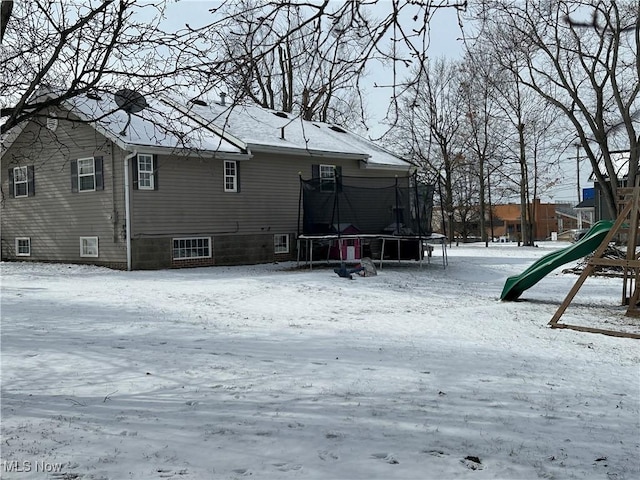 snow covered back of property featuring a playground and a trampoline