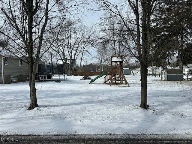 yard covered in snow with a shed, a playground, and a trampoline