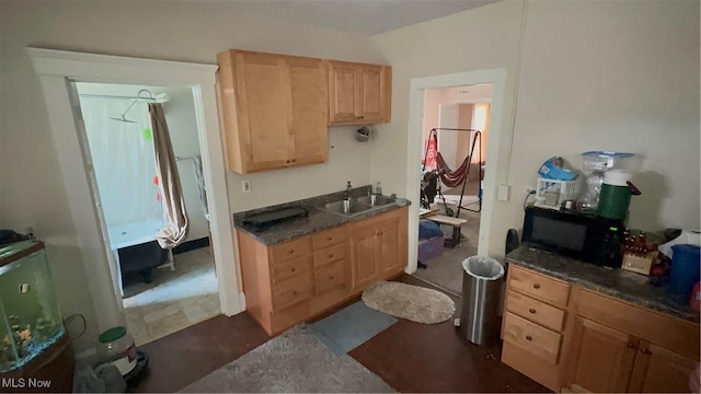 kitchen with black microwave, dark countertops, a sink, and light brown cabinets