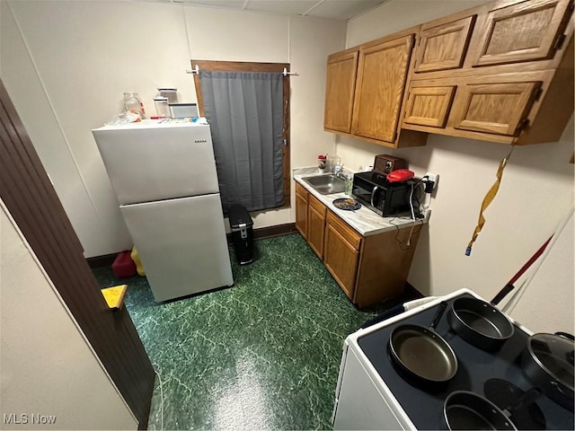 kitchen with light countertops, a sink, freestanding refrigerator, black microwave, and brown cabinetry
