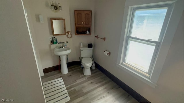 bathroom with baseboards, wood finished floors, a healthy amount of sunlight, and toilet