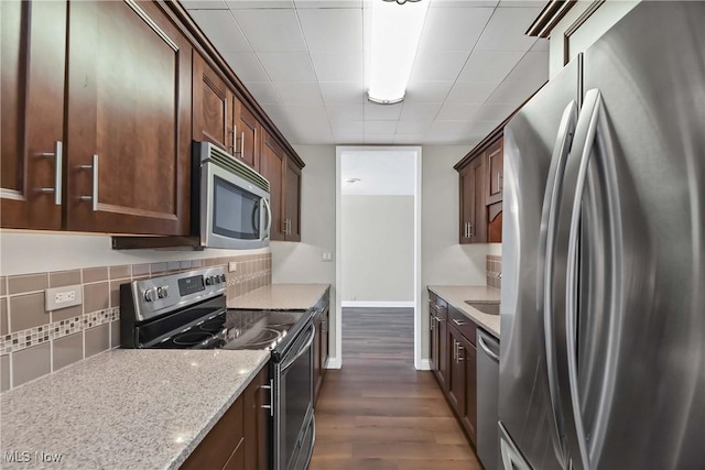 kitchen with dark wood-type flooring, dark brown cabinetry, stainless steel appliances, light stone countertops, and decorative backsplash