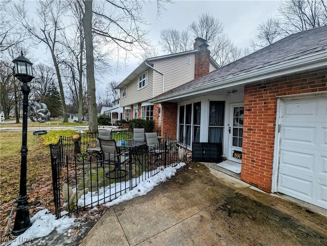 exterior space with brick siding, roof with shingles, a chimney, an attached garage, and fence