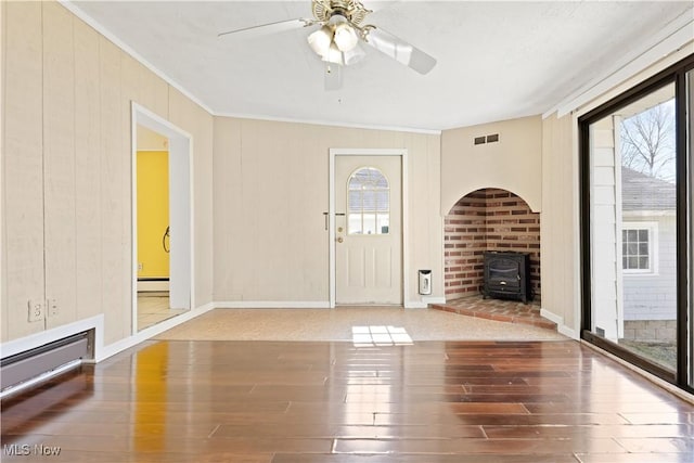 foyer with wood finished floors, a baseboard heating unit, a wood stove, ornamental molding, and visible vents