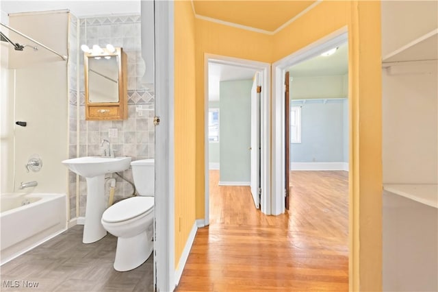 bathroom with toilet, crown molding, wood finished floors, baseboards, and bathing tub / shower combination