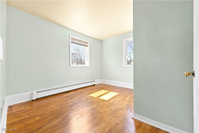 unfurnished room featuring baseboard heating, baseboards, and hardwood / wood-style floors