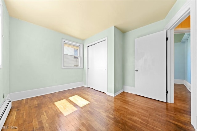 unfurnished bedroom with a baseboard heating unit, baseboards, a closet, and wood-type flooring