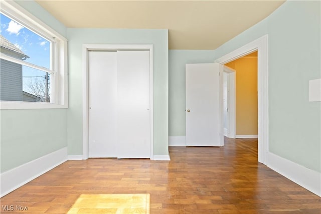 unfurnished bedroom featuring wood finished floors, a closet, and baseboards