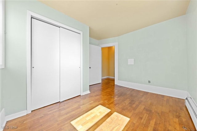 unfurnished bedroom featuring a baseboard radiator, light wood-style floors, a closet, and baseboards