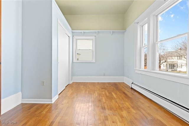 interior space featuring baseboard heating, multiple windows, light wood-style floors, and a closet