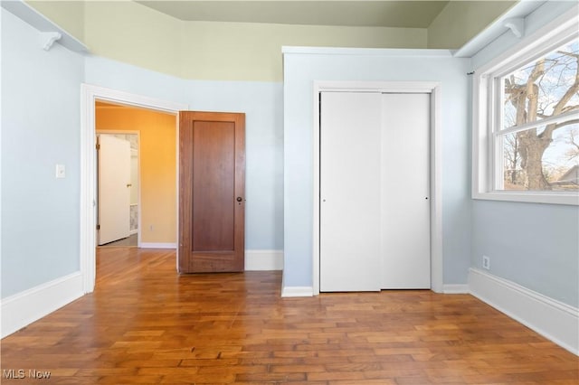 unfurnished bedroom featuring baseboards, wood finished floors, and a closet