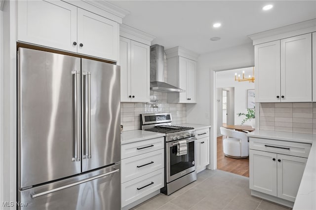 kitchen with white cabinetry, stainless steel appliances, wall chimney exhaust hood, light stone countertops, and decorative backsplash