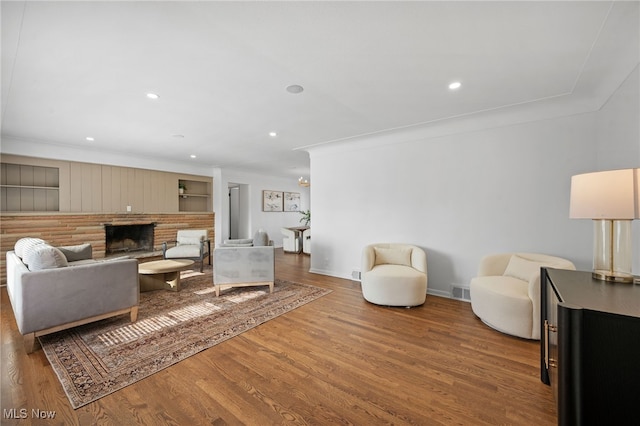 living room featuring a brick fireplace, ornamental molding, and wood-type flooring