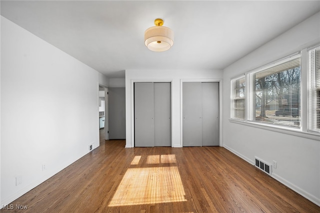 unfurnished bedroom featuring hardwood / wood-style flooring and two closets