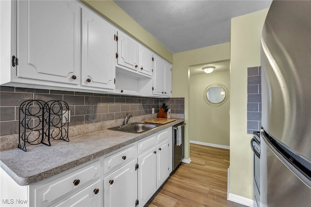 kitchen with white cabinetry, light wood-type flooring, sink, appliances with stainless steel finishes, and decorative backsplash