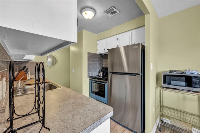 kitchen featuring tasteful backsplash, light wood-type flooring, stainless steel appliances, sink, and white cabinetry