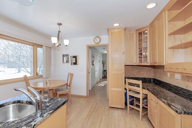 kitchen featuring dark stone countertops, sink, decorative light fixtures, built in desk, and light brown cabinetry