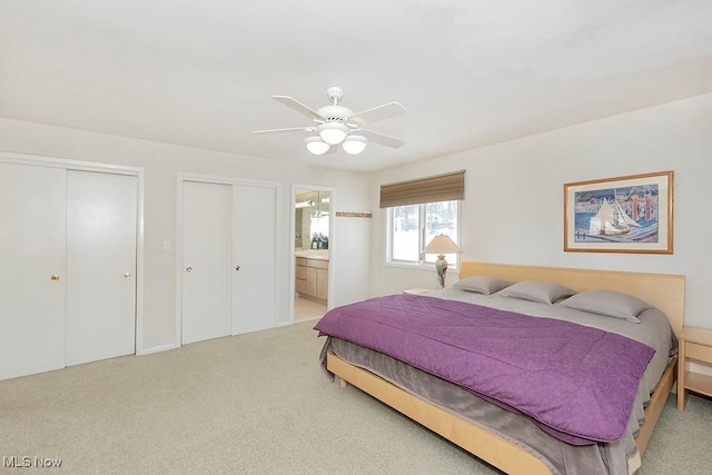 bedroom with ceiling fan, two closets, ensuite bath, and light carpet