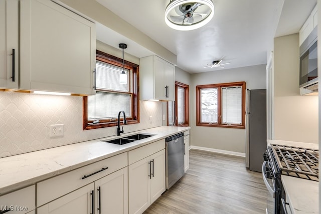 kitchen with stainless steel appliances, decorative light fixtures, sink, light stone counters, and white cabinets