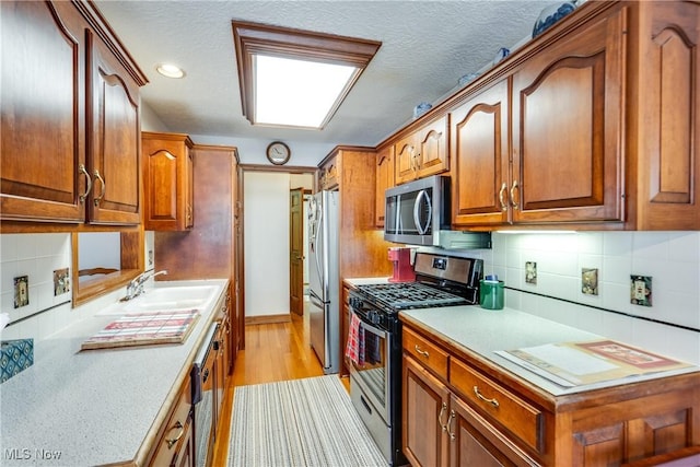 kitchen featuring stainless steel appliances, light hardwood / wood-style floors, sink, a textured ceiling, and decorative backsplash