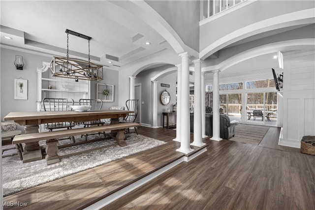 dining area featuring decorative columns, a towering ceiling, dark hardwood / wood-style floors, and a raised ceiling