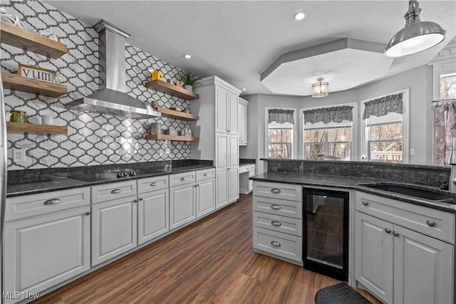 kitchen with wall chimney exhaust hood, black electric cooktop, beverage cooler, dark hardwood / wood-style flooring, and sink