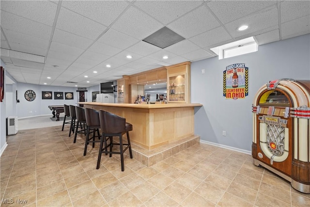 kitchen featuring kitchen peninsula, light tile patterned flooring, a breakfast bar area, and a drop ceiling