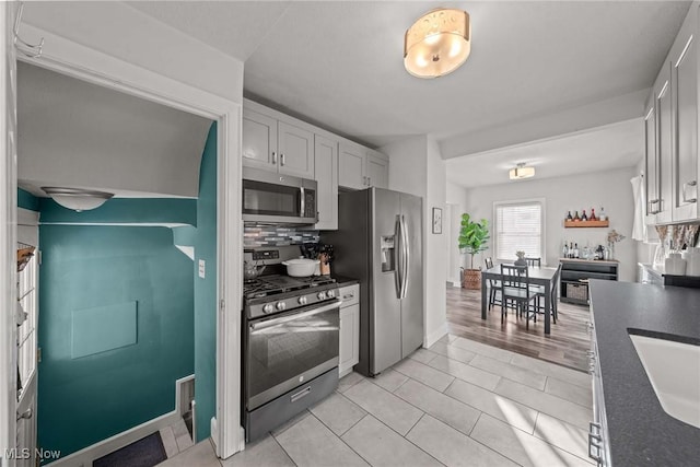 kitchen with appliances with stainless steel finishes, light tile patterned flooring, tasteful backsplash, and white cabinets