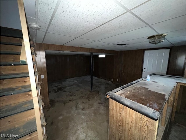 basement with wooden walls and a drop ceiling