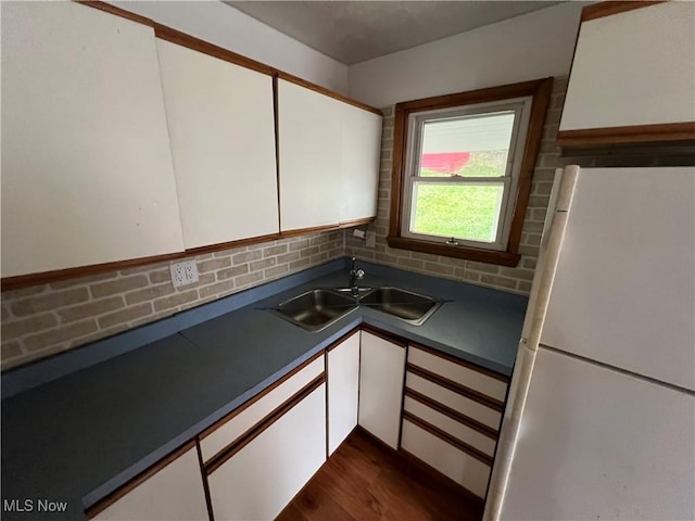 kitchen featuring white cabinetry, white refrigerator, sink, dark wood-type flooring, and decorative backsplash