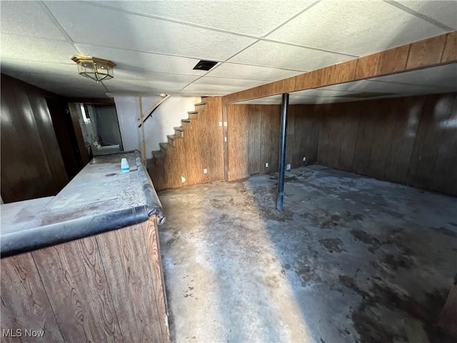 basement with a paneled ceiling and wood walls